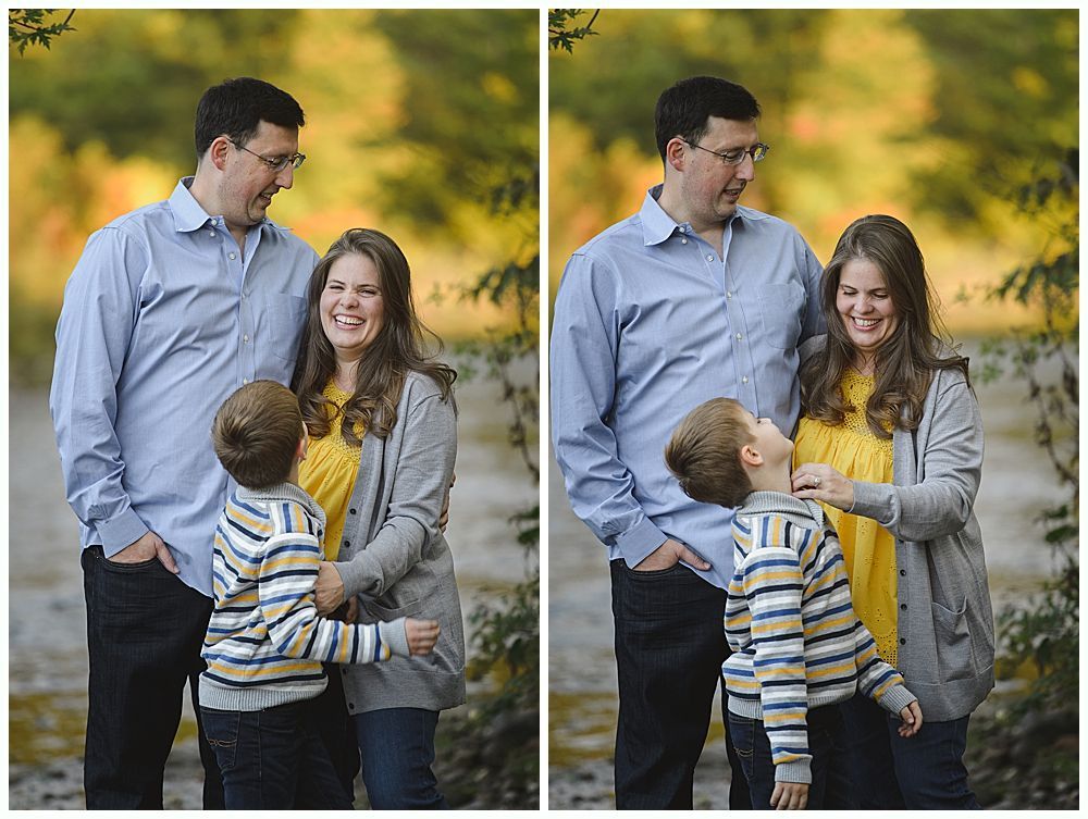 Family of three smiles outdoors near water. Son hugs mother, then looks up at her as she touches his face.