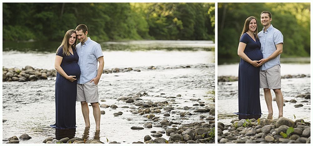 Pregnant couple stands in a river, embracing. Woman in a dark blue dress, man in a light blue shirt and shorts.