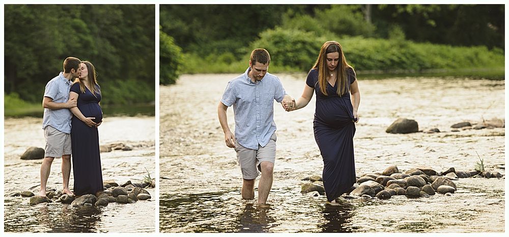 Pregnant couple wading in a shallow river, holding hands, with green foliage in background.