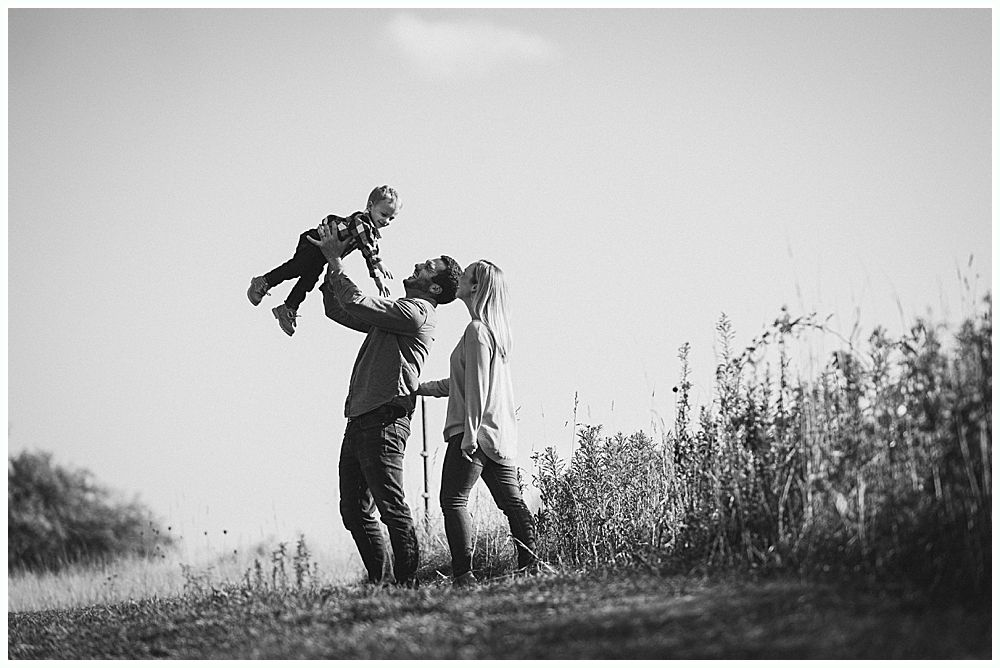 A father throws a child up in the air as the mother stands by, outdoors in black and white.