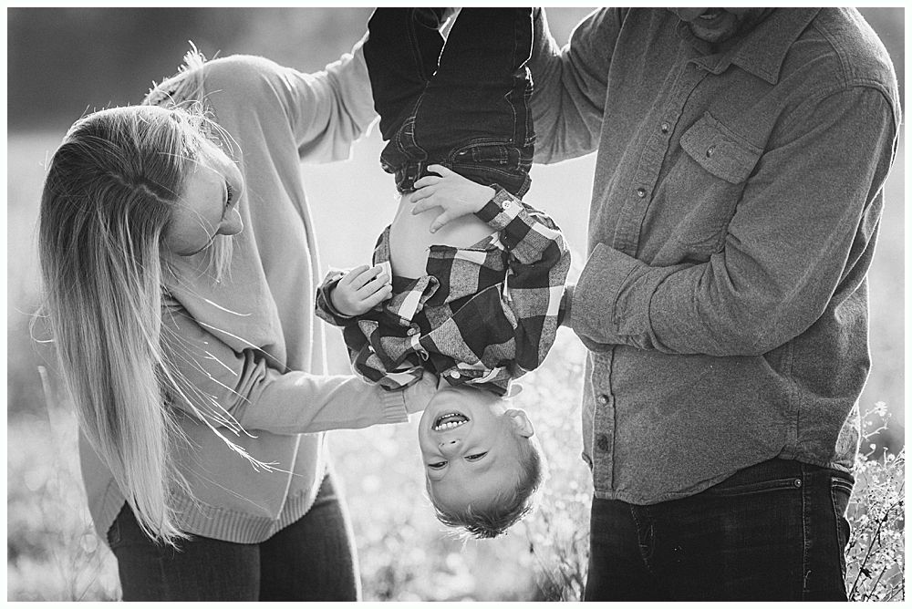 Parents holding a child upside down, smiling. Outdoor setting. Black and white.