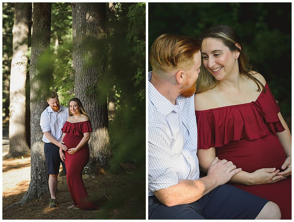 Pregnant woman in red dress with man in a forest, holding her belly and smiling.