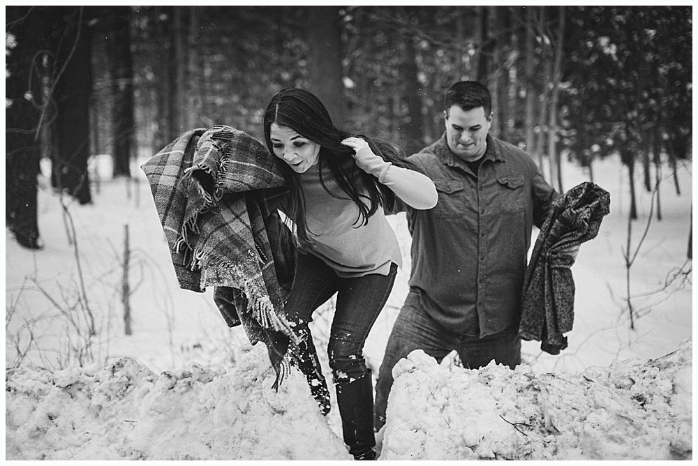 Couple walking through snow-covered woods, carrying blankets.