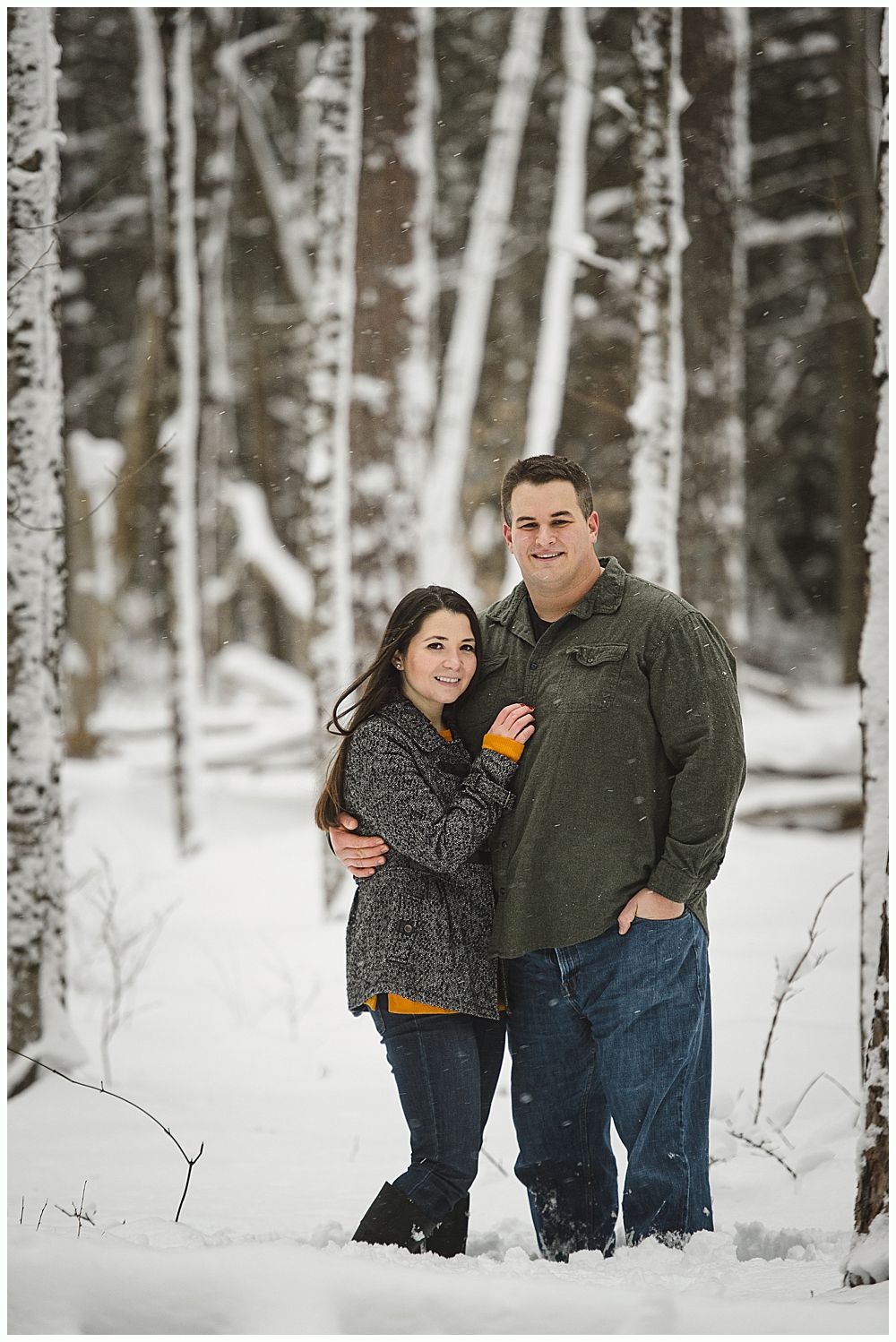 Couple standing in a snowy forest, man with arm around woman.