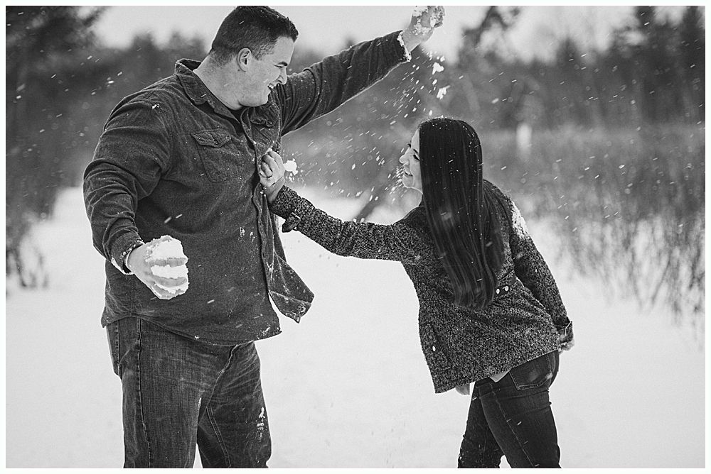 Man and person in winter jackets playfully throw snow at each other on a snow-covered path.