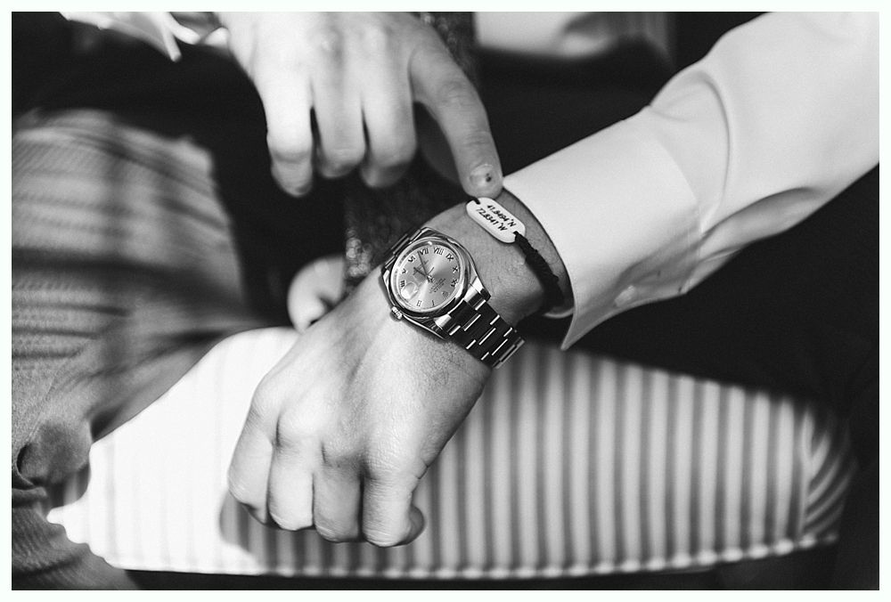 A person's wrist with a wristwatch and a small white sensor bracelet; a finger touches the sensor.