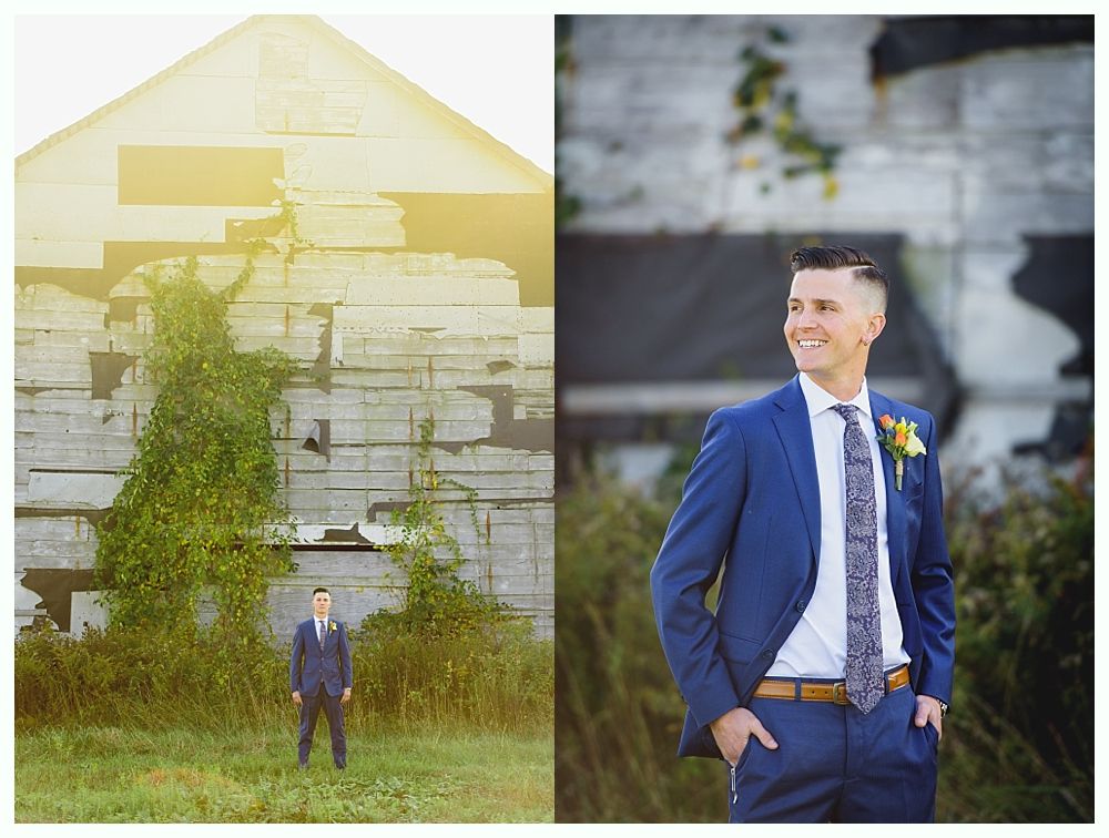 Man in blue suit stands in front of a weathered building. He smiles, hands in pockets.