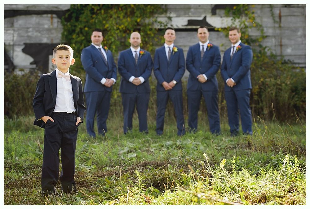Boy in suit with hands in pockets stands before five men in suits, all on grassy ground.