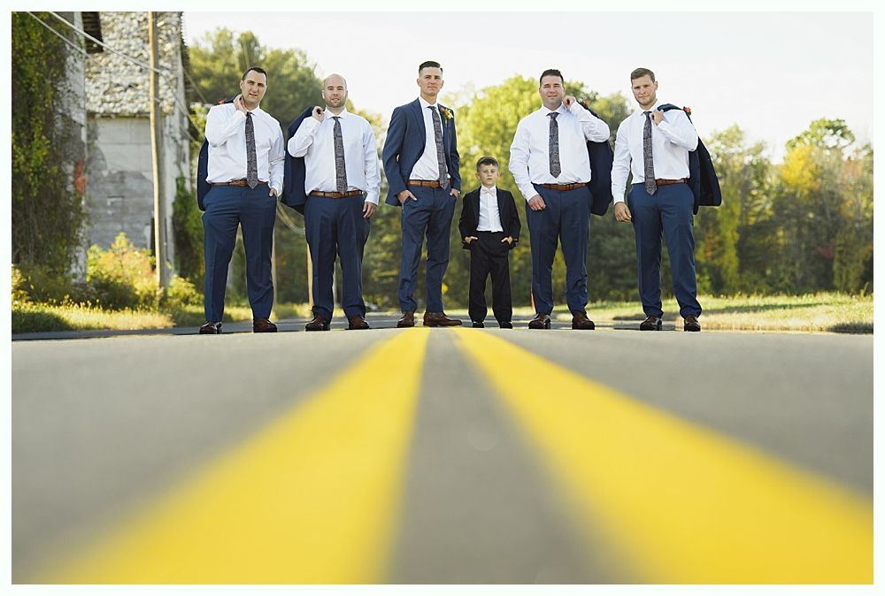Groomsmen and a young boy stand on a road with yellow lines, wearing suits and looking at the camera.