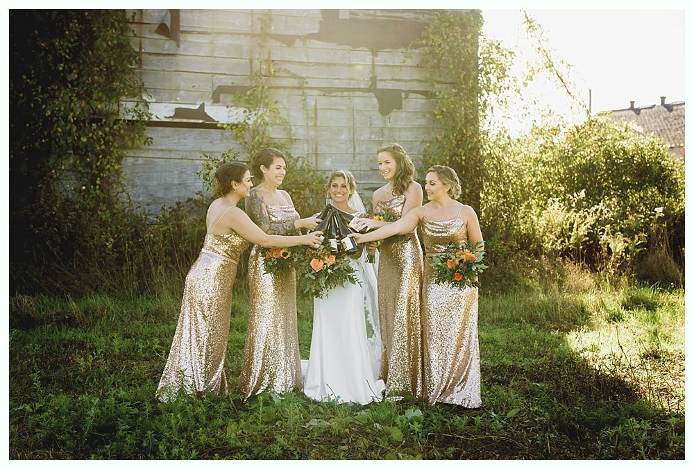 Bride with bridesmaids in gold gowns holding bouquets outdoors.