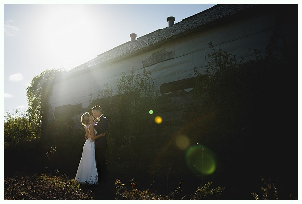 Couple in wedding attire embrace in front of an old, sunlit building.