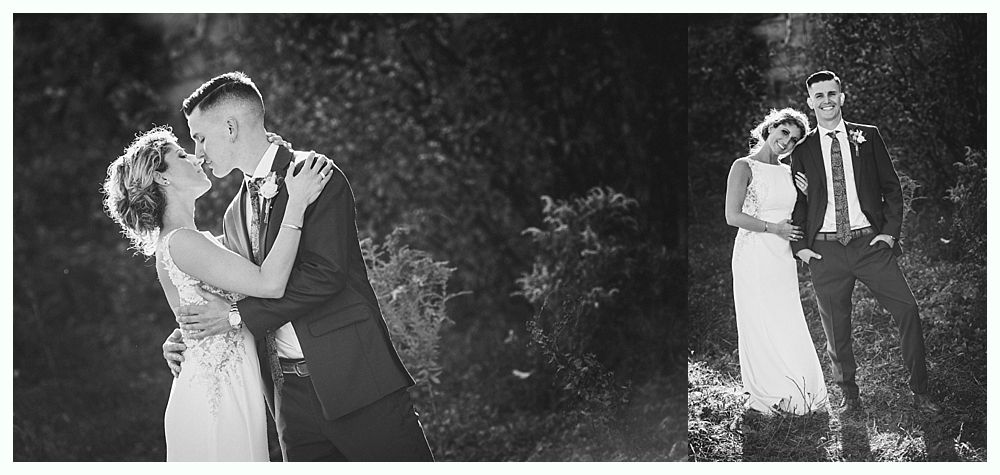 Black and white wedding photo of a couple kissing and then smiling together amongst greenery.