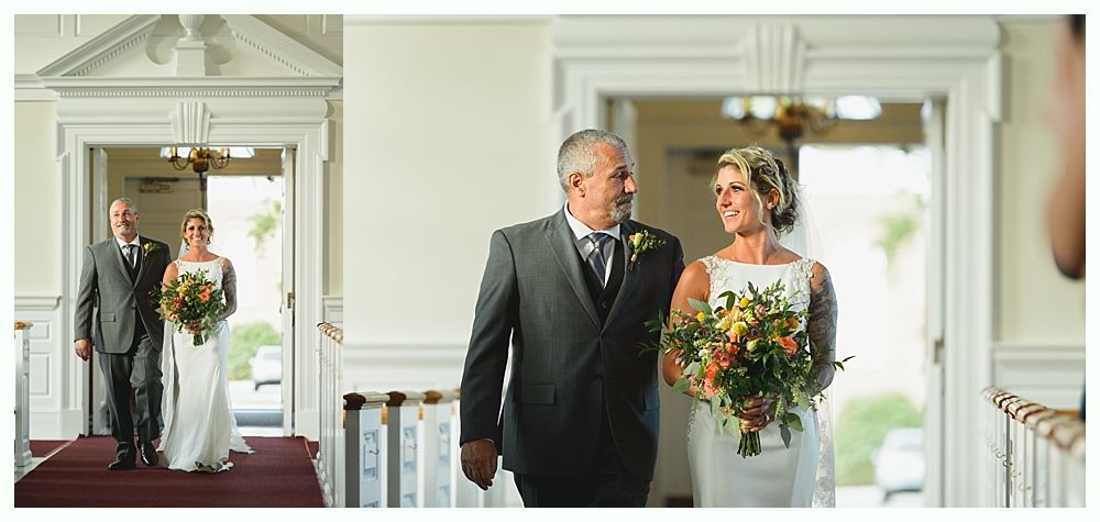 Bride and her father walking towards the camera through a doorway during a wedding. They are smiling.