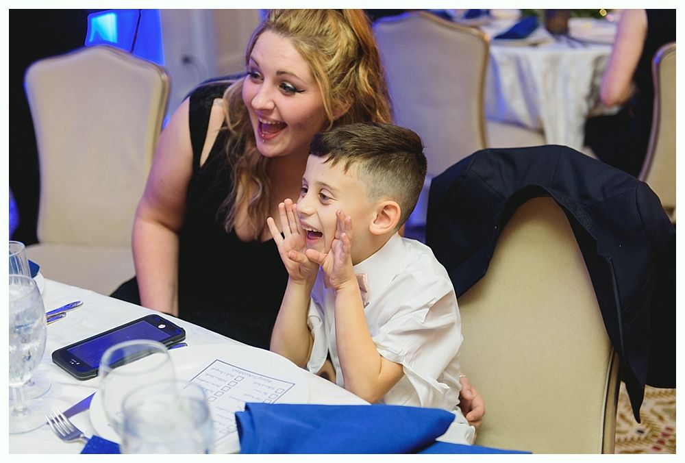 Woman and child reacting excitedly at a table, both smiling with hands near their faces.