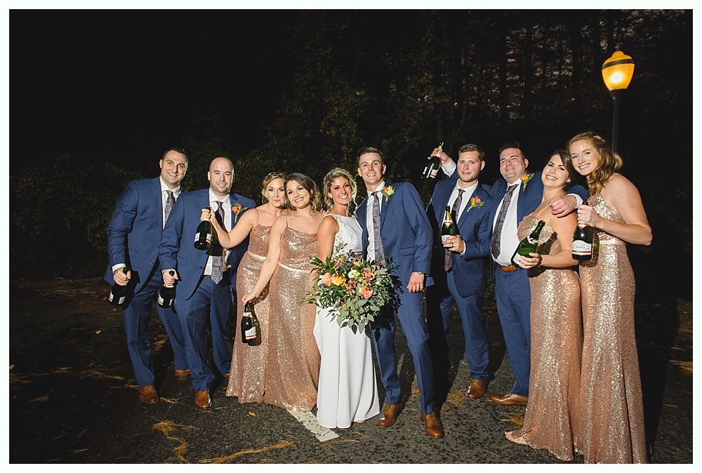 Wedding party: couple and attendants posing with champagne bottles. Night setting, gold and blue attire.