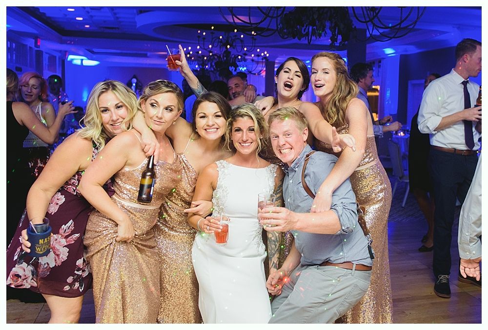 Group of people, including a bride and groom, celebrating at a party with drinks and smiles.