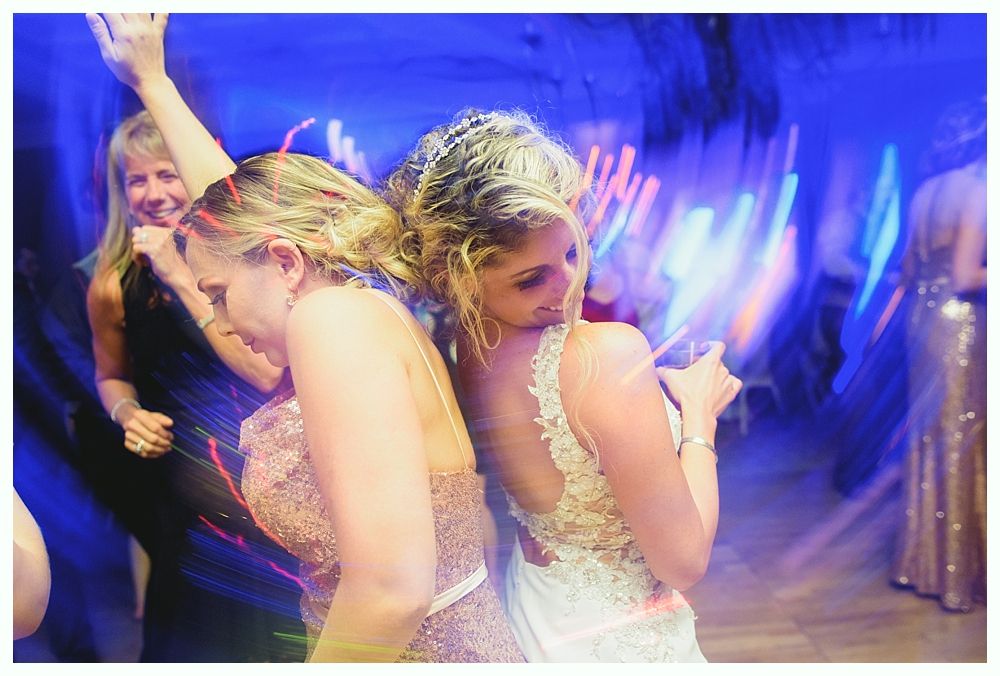 People dancing at a party with blue lighting. Two women face away, close together, while dancing.