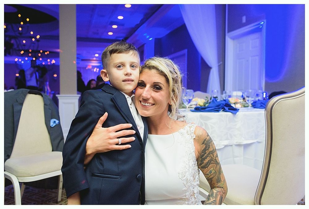 Woman with blonde hair and a boy in a suit, both smiling, pose for a photo in a room with blue lighting.