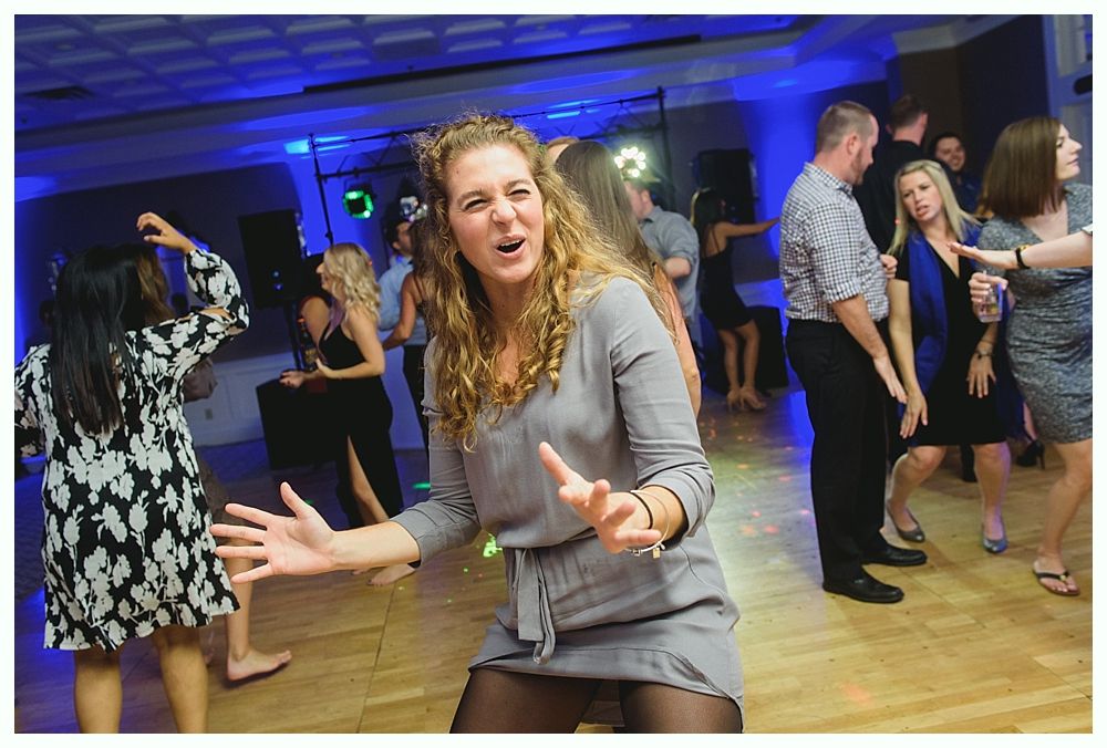 Woman dancing enthusiastically at a party, surrounded by others on a dance floor with colorful lights.