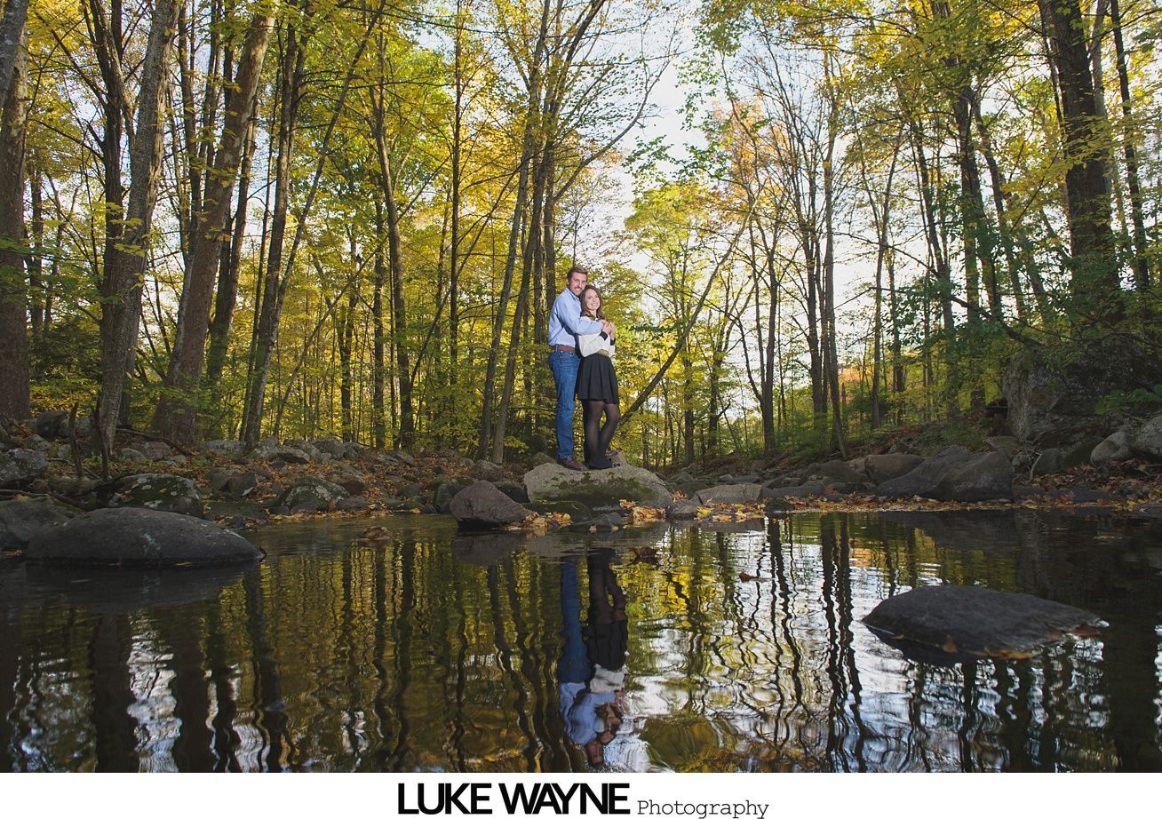 Couple poses in stone archway, framed by columns and greenery. Man in blue shirt, woman in patterned dress.