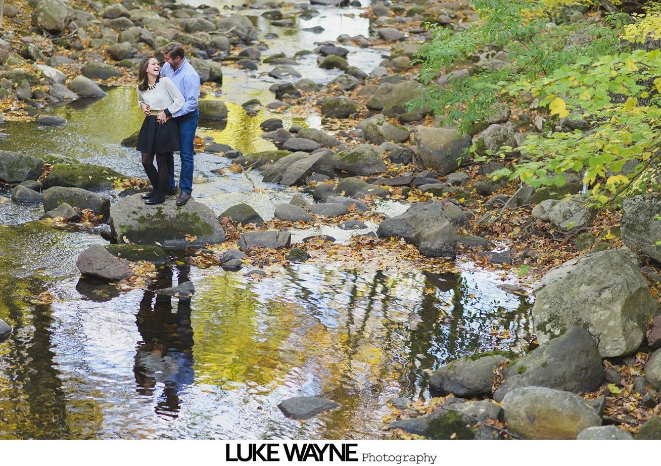 Woman resting her head on a man's chest; smiling, outdoors, in front of greenery.