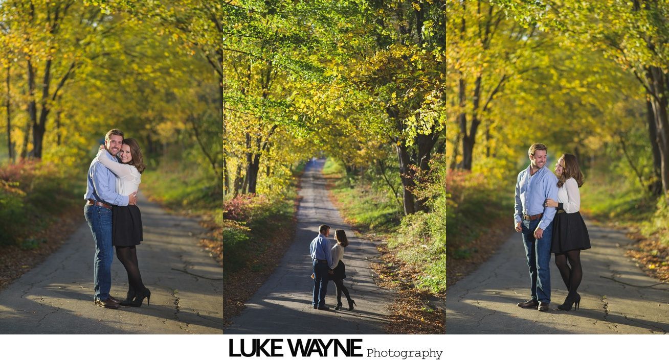 Couple holds hands and runs down a dirt path, woman laughing, man smiling, green grass, trees in background.