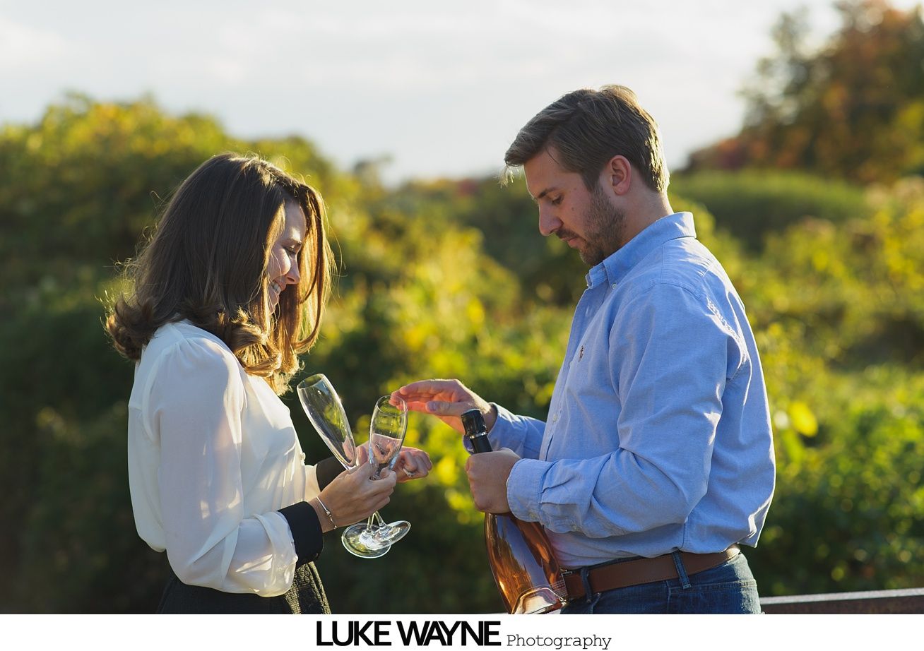 Couple holding hands, jumping on a gravel road. Woman in white pants, turquoise shirt. Man in khaki shorts, navy polo.