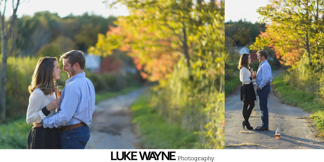 Man hugging woman from behind on a beach, both smiling. The woman shows off a ring.