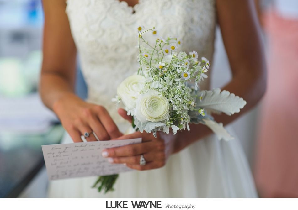 Bride in white dress holding a bouquet and a handwritten note, close-up shot.