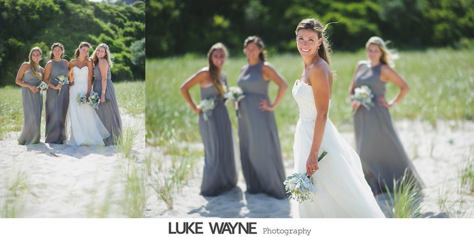 Bride and bridesmaids in gray dresses pose on a sandy beach, sunny day.