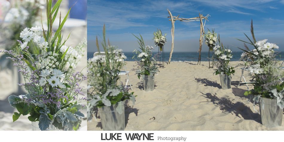 Beach wedding ceremony with white flowers, wooden archway, and sandy aisle.