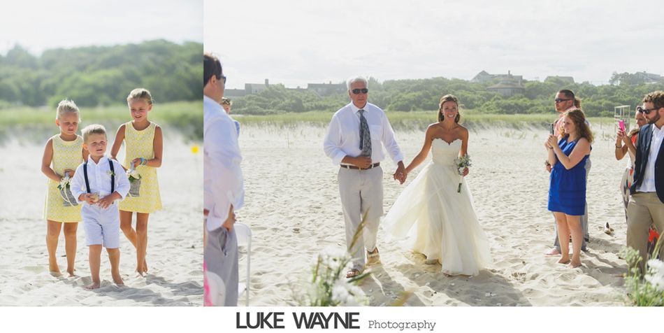 Bride and father walk down beach aisle after wedding ceremony. Guests clap; yellow dresses; sunny day.