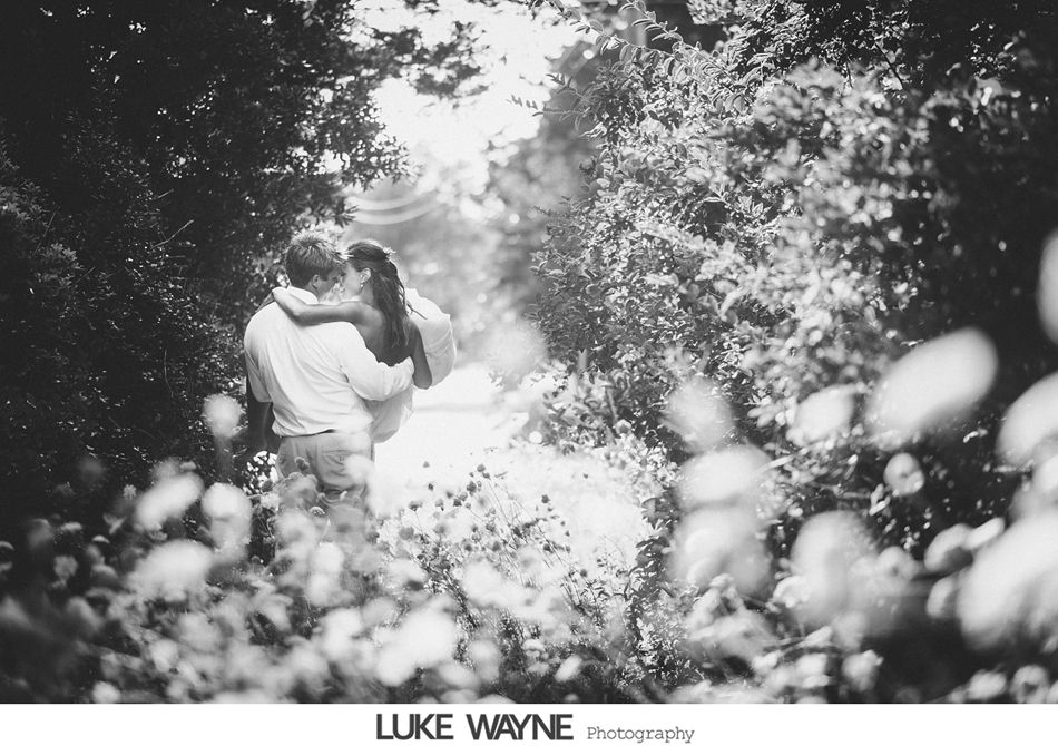Couple embracing and kissing amidst foliage. Black and white photograph, outdoor setting.