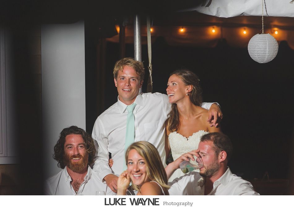 Wedding group portrait: Bride and groom smile, posing with friends on a boat at night.