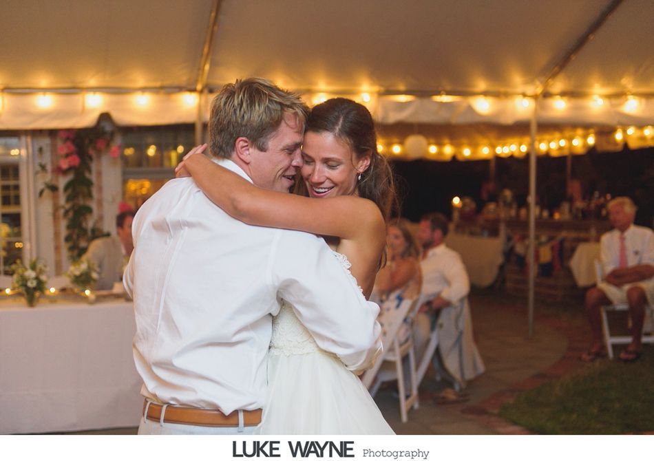 Couple dancing at a wedding reception under string lights. The woman smiles, embracing her partner.