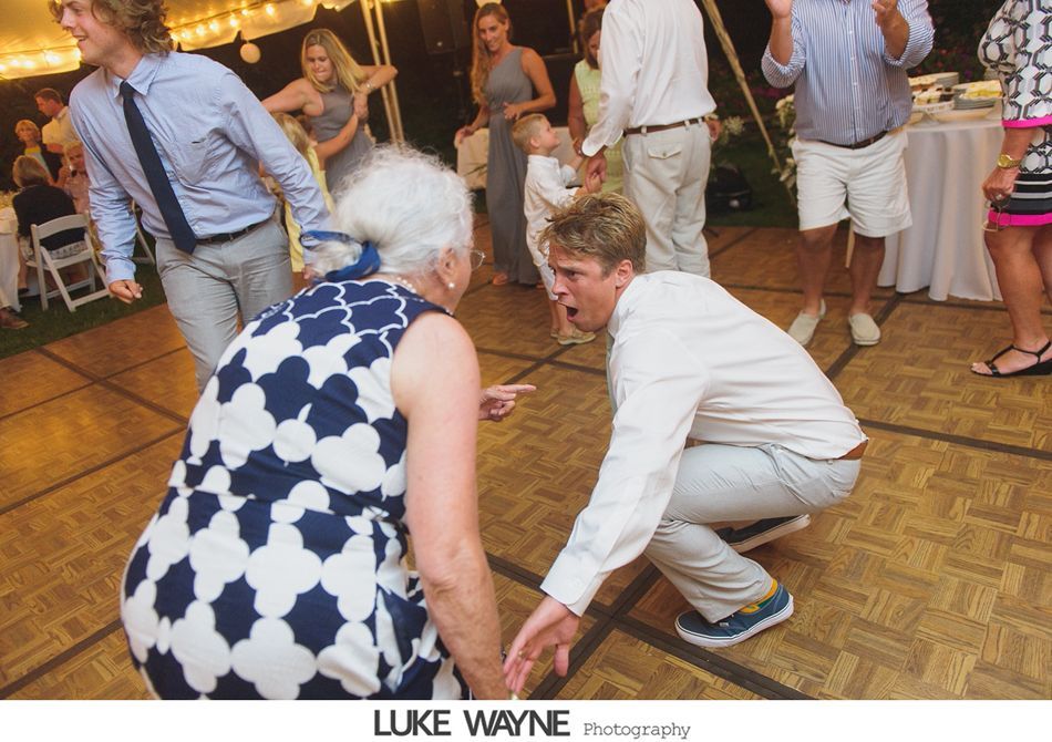 A woman and a man dance on a wooden floor at an outdoor event. They are facing each other, pointing and laughing.