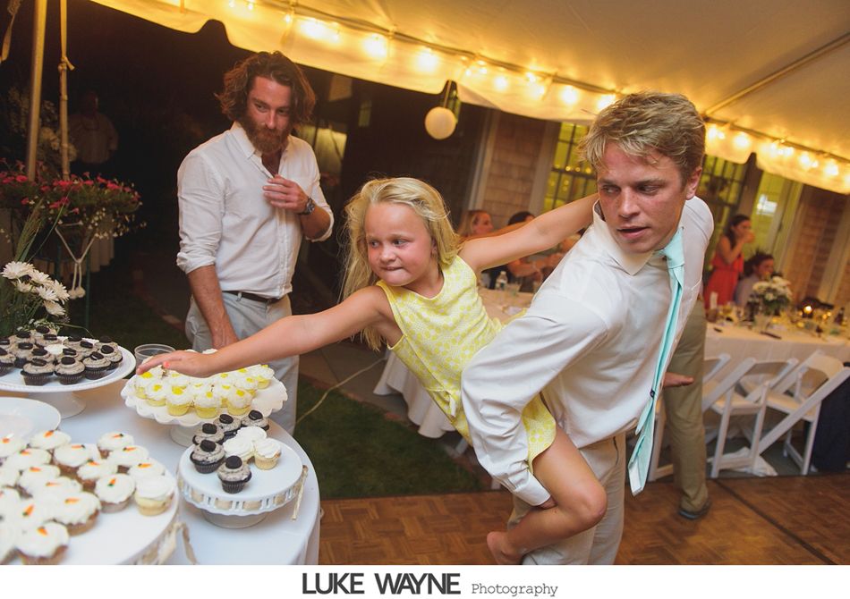 A man carries a young girl away from a dessert table at an outdoor event. Another man watches.