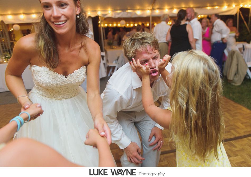 Bride laughs as children play with groom at outdoor wedding reception.