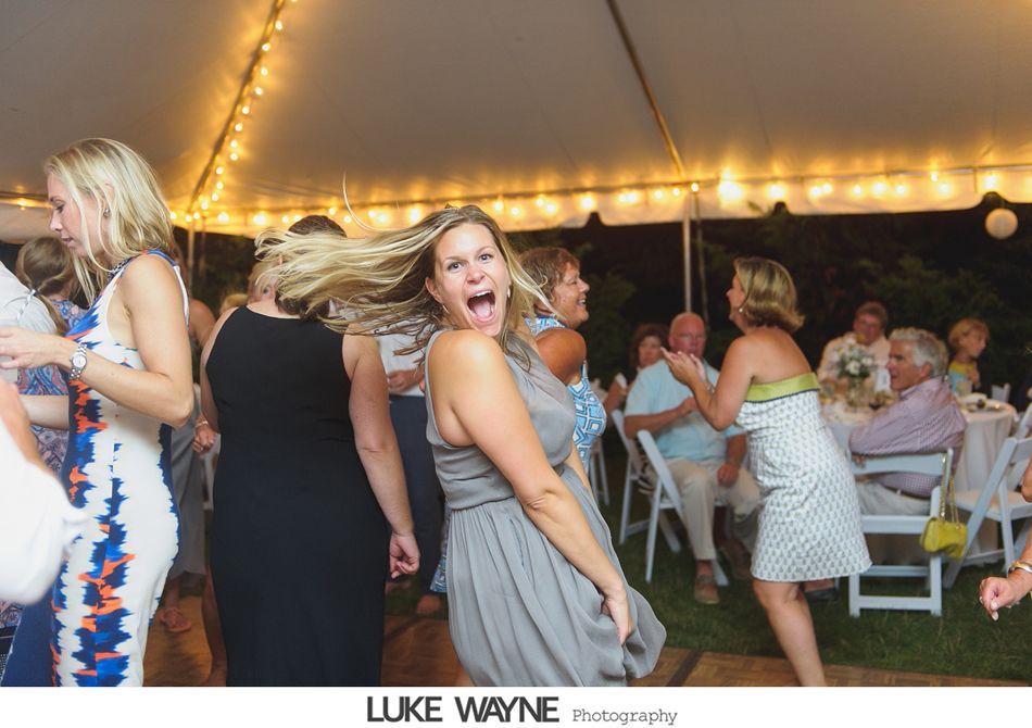 Guests dancing and laughing at an outdoor wedding reception under a lit tent.