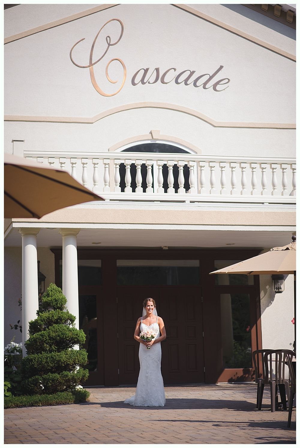 Couple on boardwalk by ocean, framed by beach plants under a blue sky with clouds.