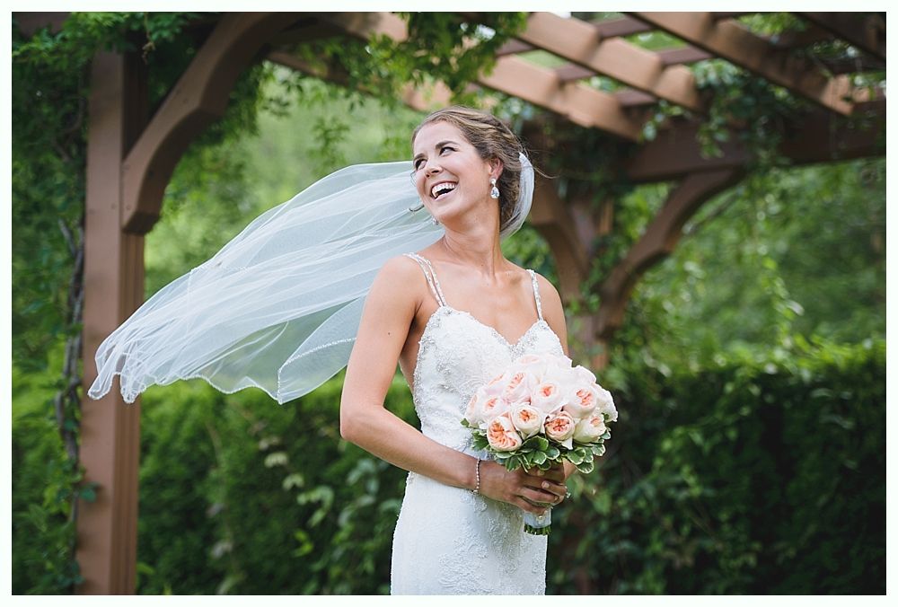 Bride and groom embrace on rocks by the ocean at sunset. The groom wears a blue suit, the bride a white dress.