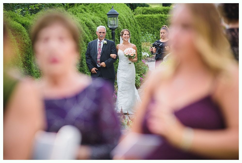 Bride with arms up, making a funny face, groom looking at his hand, cake cutting in background.