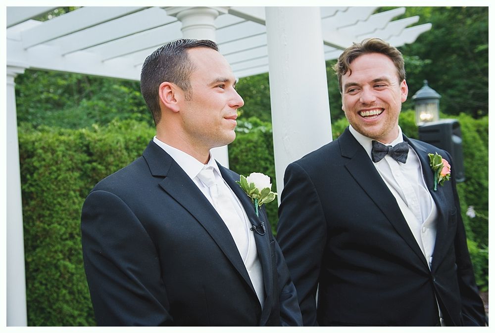 Bride with arms up, making a funny face, groom looking at his hand, cake cutting in background.