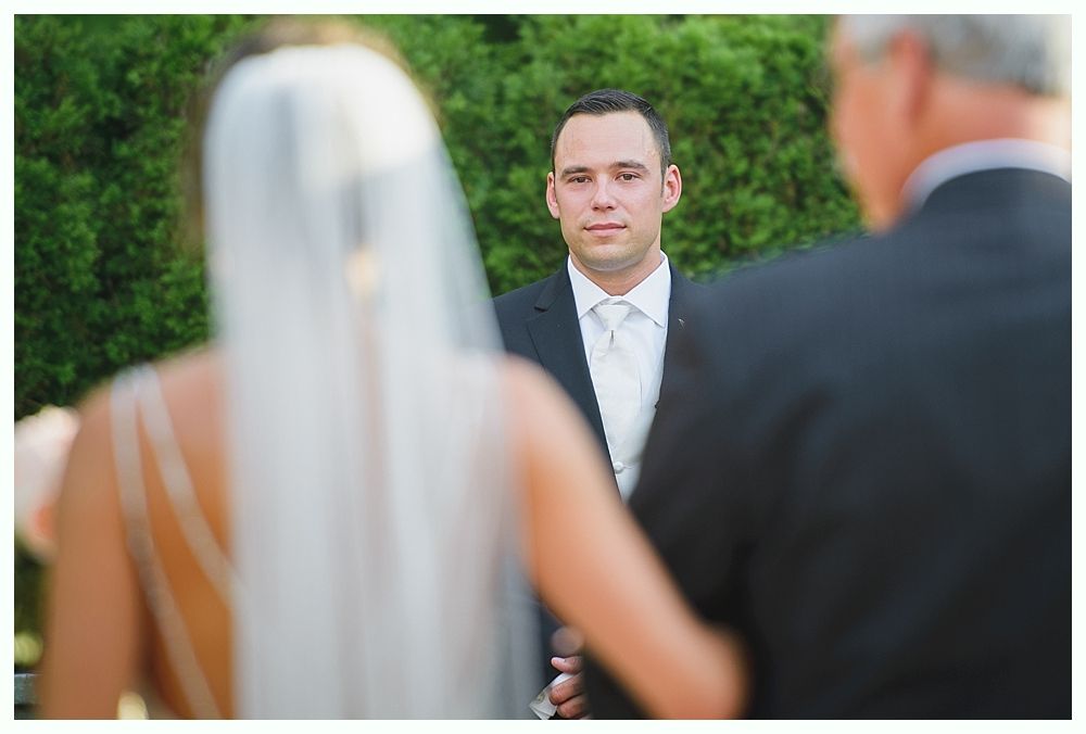 Bride with arms up, making a funny face, groom looking at his hand, cake cutting in background.