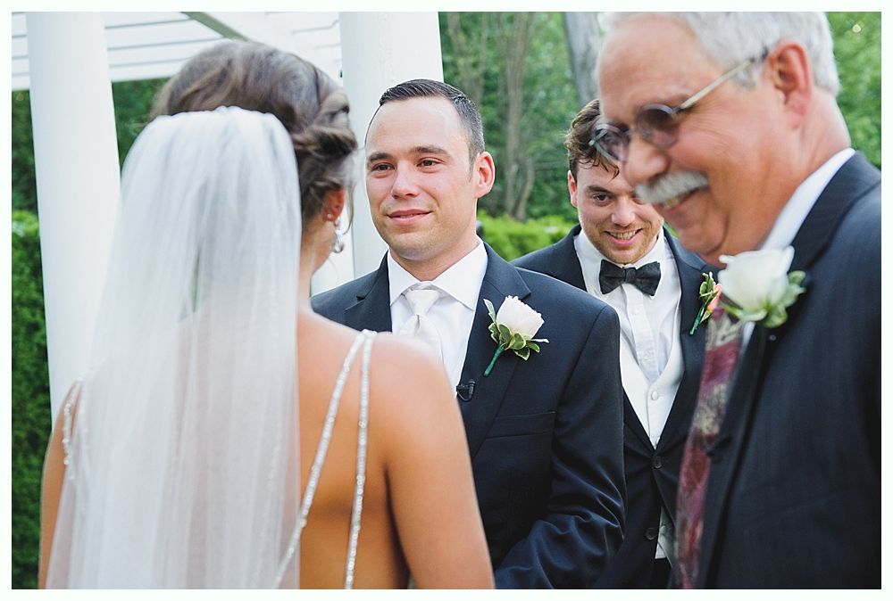 Bride with arms up, making a funny face, groom looking at his hand, cake cutting in background.