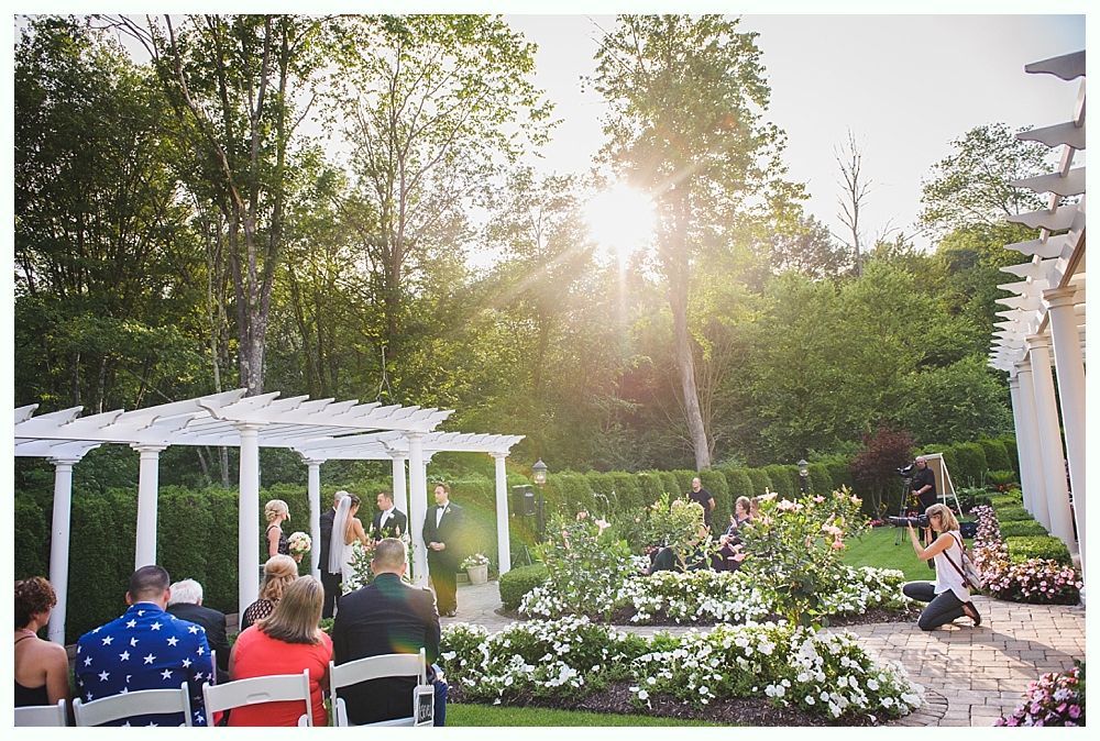 Bride with arms up, making a funny face, groom looking at his hand, cake cutting in background.