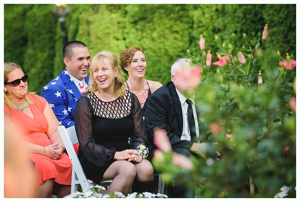 Bride with arms up, making a funny face, groom looking at his hand, cake cutting in background.