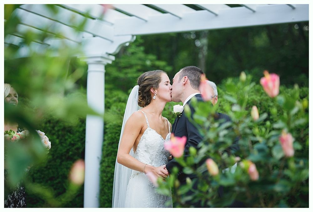 Bride with arms up, making a funny face, groom looking at his hand, cake cutting in background.