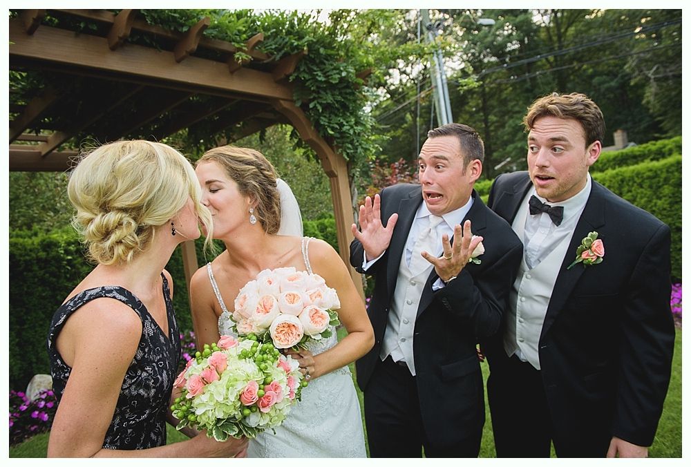 Bride with arms up, making a funny face, groom looking at his hand, cake cutting in background.