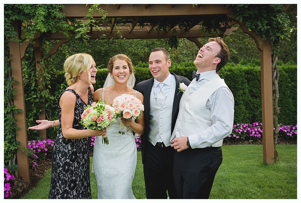 Bride with arms up, making a funny face, groom looking at his hand, cake cutting in background.